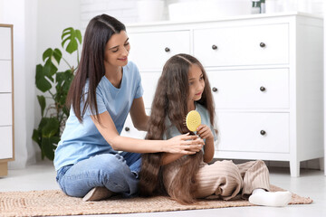 Young mother helping her little daughter brush hair while sitting on floor in bathroom