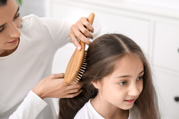 Fototapeta premium Young mother brushing hair of her little daughter in bathroom, closeup