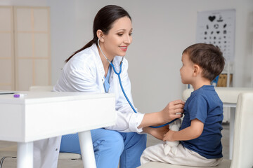 Female pediatrician with stethoscope listening to cute little boy at table in clinic