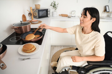Beautiful young woman in wheelchair making pancakes at home