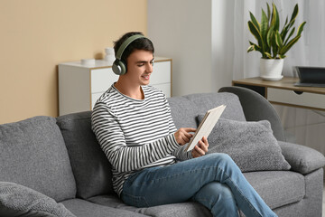 Handsome young man with headphones and tablet computer sitting on sofa at home