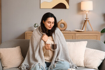 Beautiful young happy woman with cup of hot chocolate and plaid sitting on sofa at home