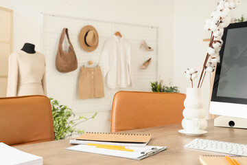 Vase with cotton flowers and coffee cup on table in clothing store office
