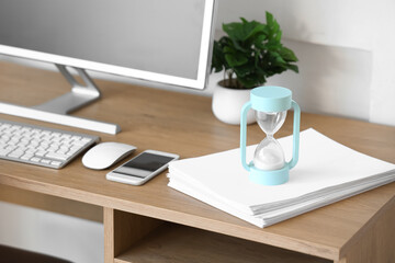 Hourglass with papers on desk in office, closeup