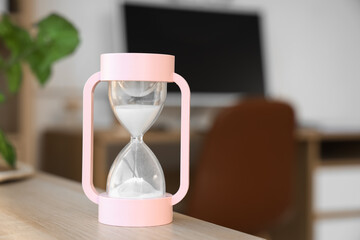 Pink hourglass on table in office, closeup