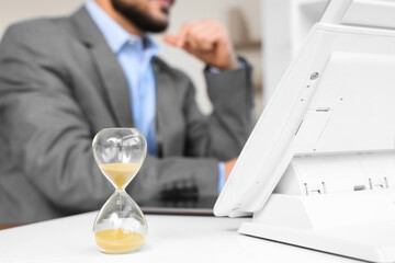 Hourglass and telephone on desk against businessman working in office, closeup