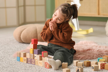Cute little girl with wooden cubes sitting on carpet in living room