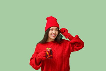 Beautiful young happy Asian woman in winter clothes with glass jar of hot mulled wine and Christmas...