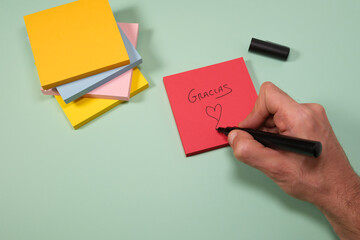 Handwriting a heart on a red sticky note with "Gracias" message