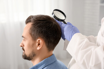 Fototapeta premium Trichologist with magnifier examining man's hair in clinic, closeup