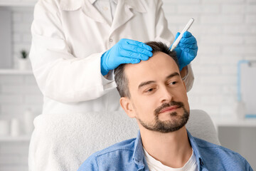 Trichologist marking man's head with hair loss problem in clinic, closeup