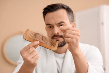 Handsome man with hair loss problem and comb in bathroom, closeup
