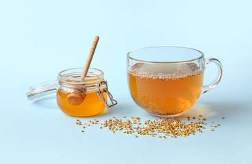 Glass cup of hot buckwheat tea and jar with honey on blue background