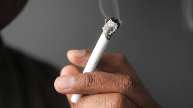 A closeup image of a hand firmly holding a smoky cigarette in detail