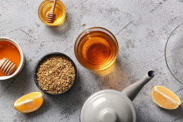Glass cup and teapot of hot buckwheat tea with lemon and bowls of honey on grunge background