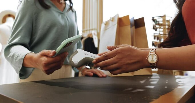 Female, fashion boutique store client paying for clothes using her phone with nfc technology while saleswoman hold card reader machine, close up shot. Transaction, contactless method payment, shopping