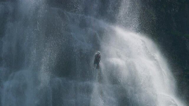 Slow motion, cinematic shot of person rappelling down massive waterfall with grace