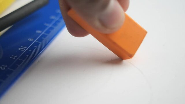 Carefully erasing pencil markings using an orange eraser on white paper