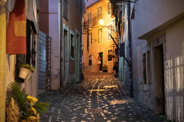 A young Portuguese woman opens her apartment door on a narrow illuminated residential alley at night in the historic medieval Alfama district of Lisbon Portugal.
