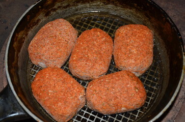 Five meat cutlets are fried in a pan.