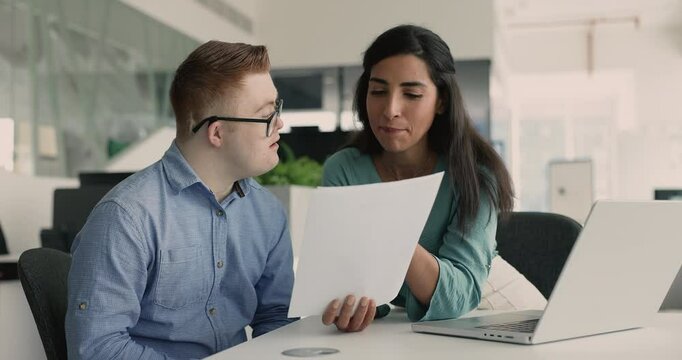 Friendly Latina female mentor training person with Down syndrome, provide structured explanations written in documents, share step-by-step instructions on paper, working together in office. Mentorship
