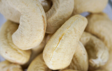 A close-up macro photograph of a handful of raw cashew nuts isolated on a white background, showcasing their natural texture, creamy color, and detailed surface. Perfect for concepts related to health