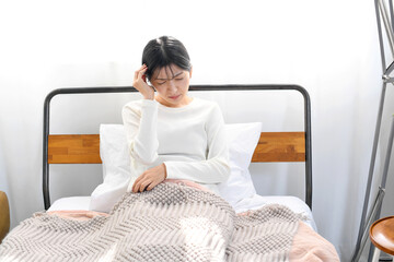 ベッドで頭痛に悩む若いアジア人女性