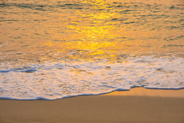 Sea waves on the beach with sunset light reflecting on the sandy beach surface in the soft evening light.