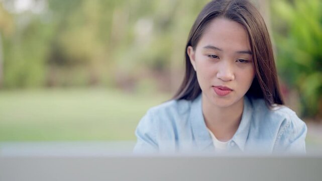 A woman is sitting in front of a laptop computer. She is looking at the screen with a serious expression on her face