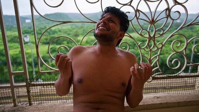 Guy without a shirt sits on balcony floor sobbing