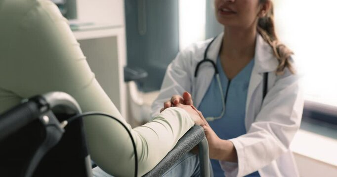 Positive female doctor consoling patient in wheelchair, touching and stroking hand with sympathy, support, telling about rehabilitation, successful therapy, optimistic diagnosis. Cropped shot