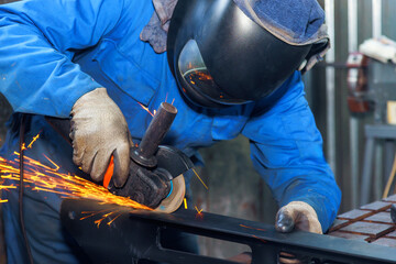 Worker in protective gear grinds metal, creating sparks in an industrial setting at metal...