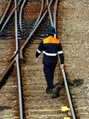 A man in a safety vest walks along a railroad track. Concept of caution and responsibility, as the...