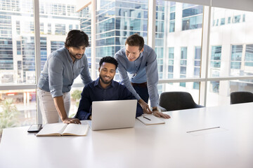 Diverse group of three business colleagues meeting at laptop, working on project together, watching...