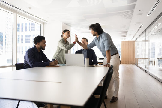 Happy Indian office colleagues clapping hands, giving high five gesture, enjoying successful cooperation, partnership, finding successful creative ideas on brainstorming meeting. Wide shot