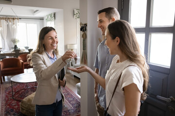 Happy successful realtor giving key to new homeowners after buying apartment, house to positive...