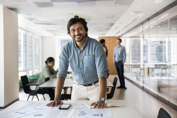 Happy Indian businessman, company owner, executive posing in open office with working team in...