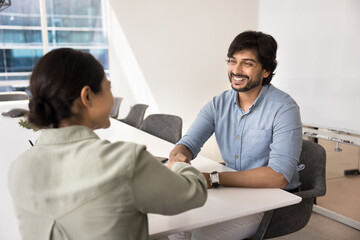 Positive confident Indian professional colleagues shaking hands after meeting, sitting at table,...