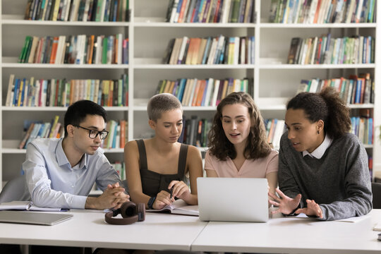 Tech and study. Four diverse multicultural schoolmates students friends using laptop in learning at college library watch video lecture search information discuss scientific article at online resource
