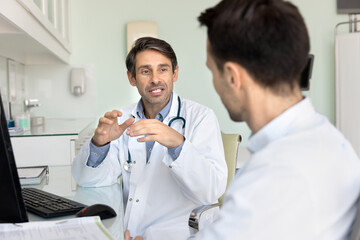 Middle aged Latin doctor meeting with colleague at workplace, talking to professional coworker,...