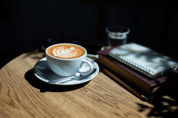 Latte coffee and reading book on wooden table with sunlight and diary for writing note, relax during a day after work in cafe