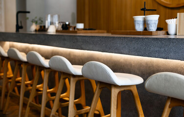 Wooden seat with cushion and coffee equipment on counter bar with wooden wall on background