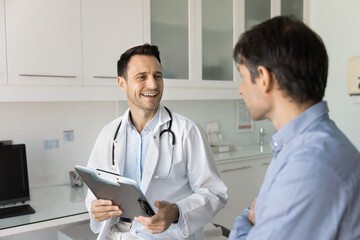 Cheerful optimistic doctor giving consultation to patient, talking to man smiling, telling good...