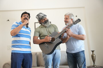 group of senior indian male friends enjoying while playing guitar and singing song at home.
