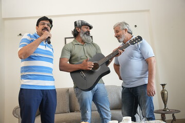 group of senior indian male friends enjoying while playing guitar and singing song at home.
