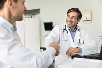 Positive successful Latin doctor giving handshake to patient at workplace, wishing getting better after optimistic treatment results, laughing. Medical professional shaking hands with colleague