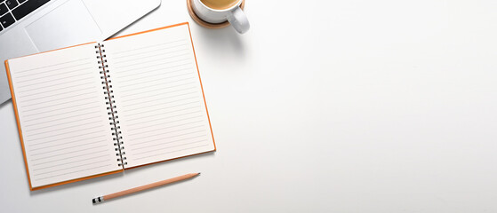 Top view of laptop, lined notebook and cup of coffee on a clean white surface