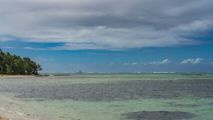 A calm turquoise ocean. Green vegetation on the shore. A boat is visible on the horizon and a...