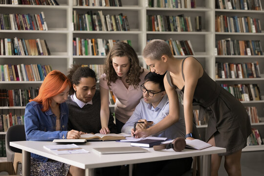 Preparing for exams. Concentrated diverse polyethnic young people students pupils group gather around desk in library collaborate in studying books search answers on test questions do research discuss