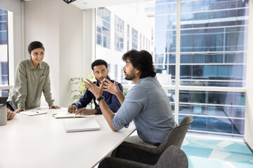 Inspired motivated Indian manager man speaking at team meeting, offering ideas for brainstorming,...